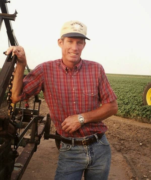 A man standing next to a tractor in the middle of a field.